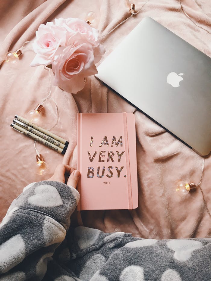 Flat lay of a cozy workspace with a pink notebook, roses, and a laptop, perfect for productivity.